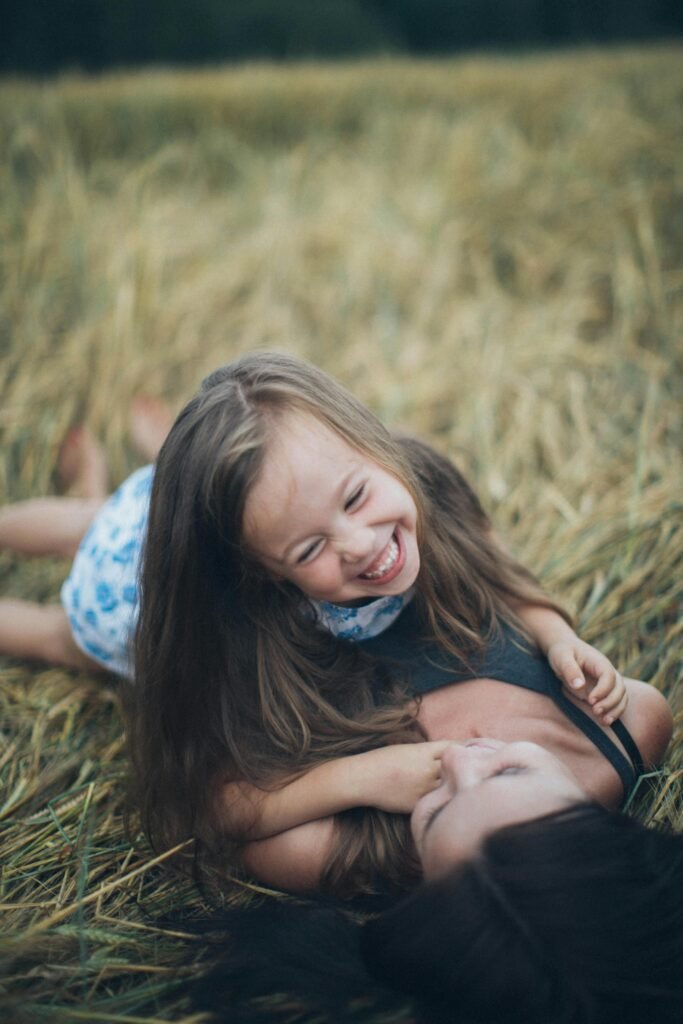 A joyful mother and daughter sharing a playful moment in a sunlit summer field.